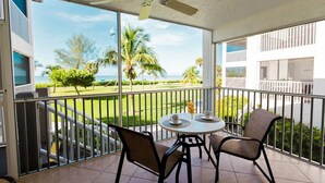 Un balcon avec une table et des chaises, un ventilateur de plafond et une vue sur une pelouse bien entretenue et des palmiers.