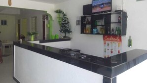 Zona de recepción de hotel con un mostrador negro, un televisor montado encima y una zona de bar con un letrero que dice 'Cocktails'.