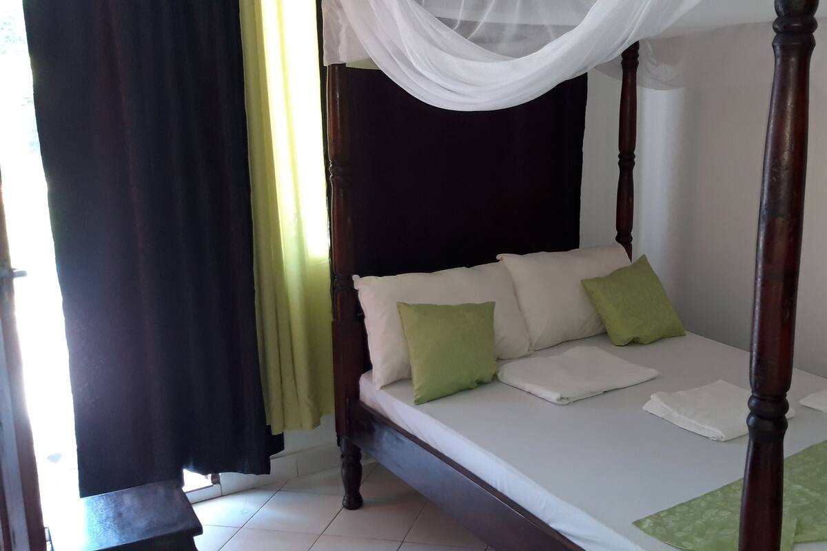 Una cama con dosel, ropa de cama blanca, almohadas verdes y una manta verde en el pie de cama.