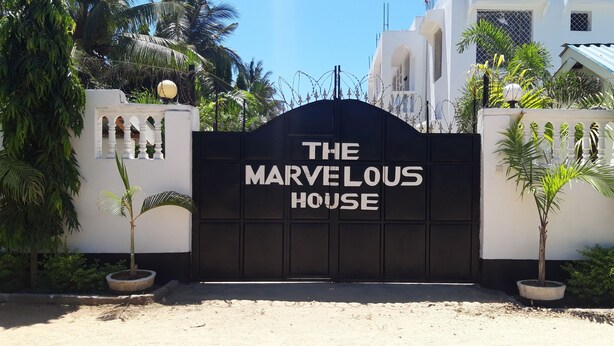 Una entrada con portón y el letrero "The Marvelous House" frente a un edificio blanco con una reja negra.