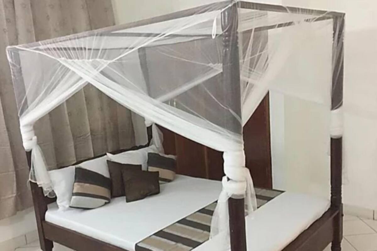Una cama con dosel y cuatro columnas, con estructura de madera y ropa de cama blanca.