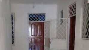 Un pasillo con puerta de madera, un portón blanco y suelo de baldosas.
