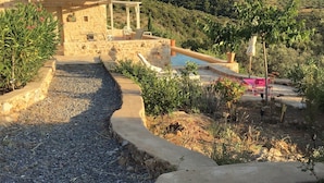 A stone building with a tiled roof, a swimming pool, and a garden area with potted plants. - Villa Luciana 'Fantastic sunsets by the pool' (Lagkada)
