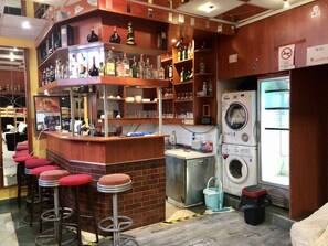 A bar area with stools, shelves of bottles, a washing machine, and a sign indicating WiFi availability.