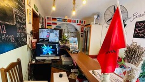 A cozy cafe with a wooden counter, a computer monitor, and a red umbrella decoration. - Vlora Backpackers Hostel (Vlorë)