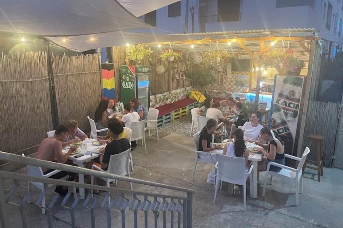 An outdoor dining area with tables and chairs, a covered seating area, and a building in the background.