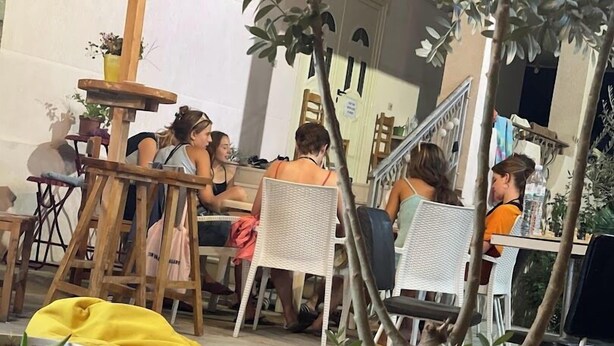 A dining area with wooden chairs and tables, potted plants, and a staircase. - Vlora Backpackers Hostel (Vlorë)