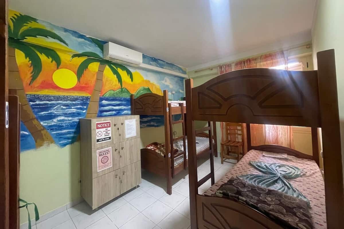 A room with bunk beds, a mural of a sunset over the ocean, a notice board, and a wooden cabinet.