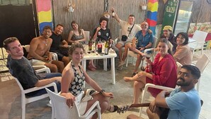A group of people seated at an outdoor table with a rustic backdrop, possibly at a restaurant or event venue. - Vlora Backpackers Hostel (Vlorë)