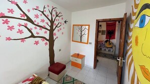 A child's room with a wall mural, a small cabinet, a patterned rug, and a doorway leading to another room. - Vlora Backpackers Hostel (Vlorë)