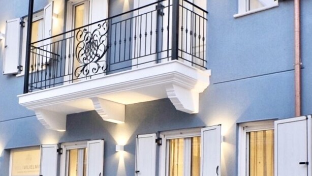 A blue building with a balcony featuring ornate black railings and white shutters. - Villa Vilielmini (Ioannina)