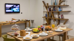 A breakfast setup with a variety of food items, a television, and a bookshelf with books and figurines. - Villa Vilielmini (Ioannina)