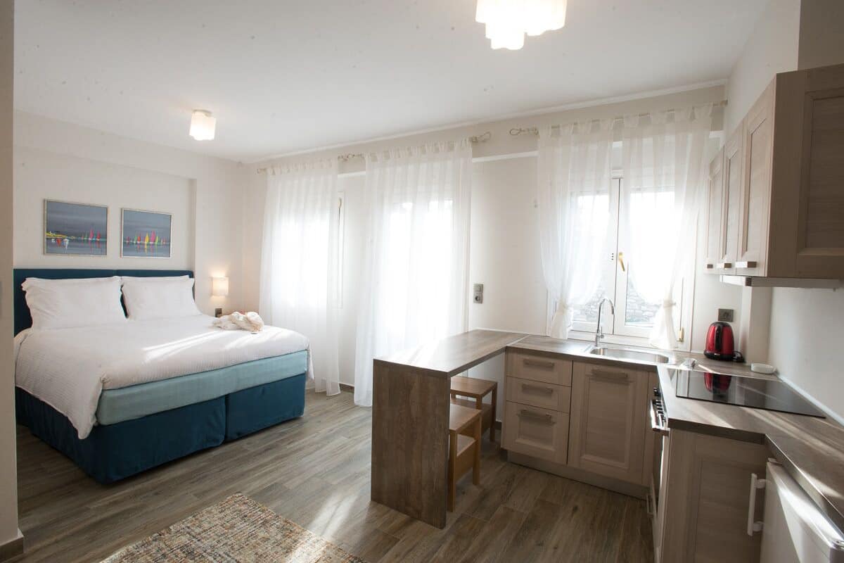 A modern hotel room with a bed, a desk, and a kitchenette.