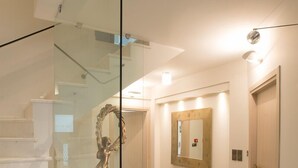 A modern interior with a glass staircase, wooden flooring, and a hallway leading to a door. - Villa Vilielmini (Ioannina)