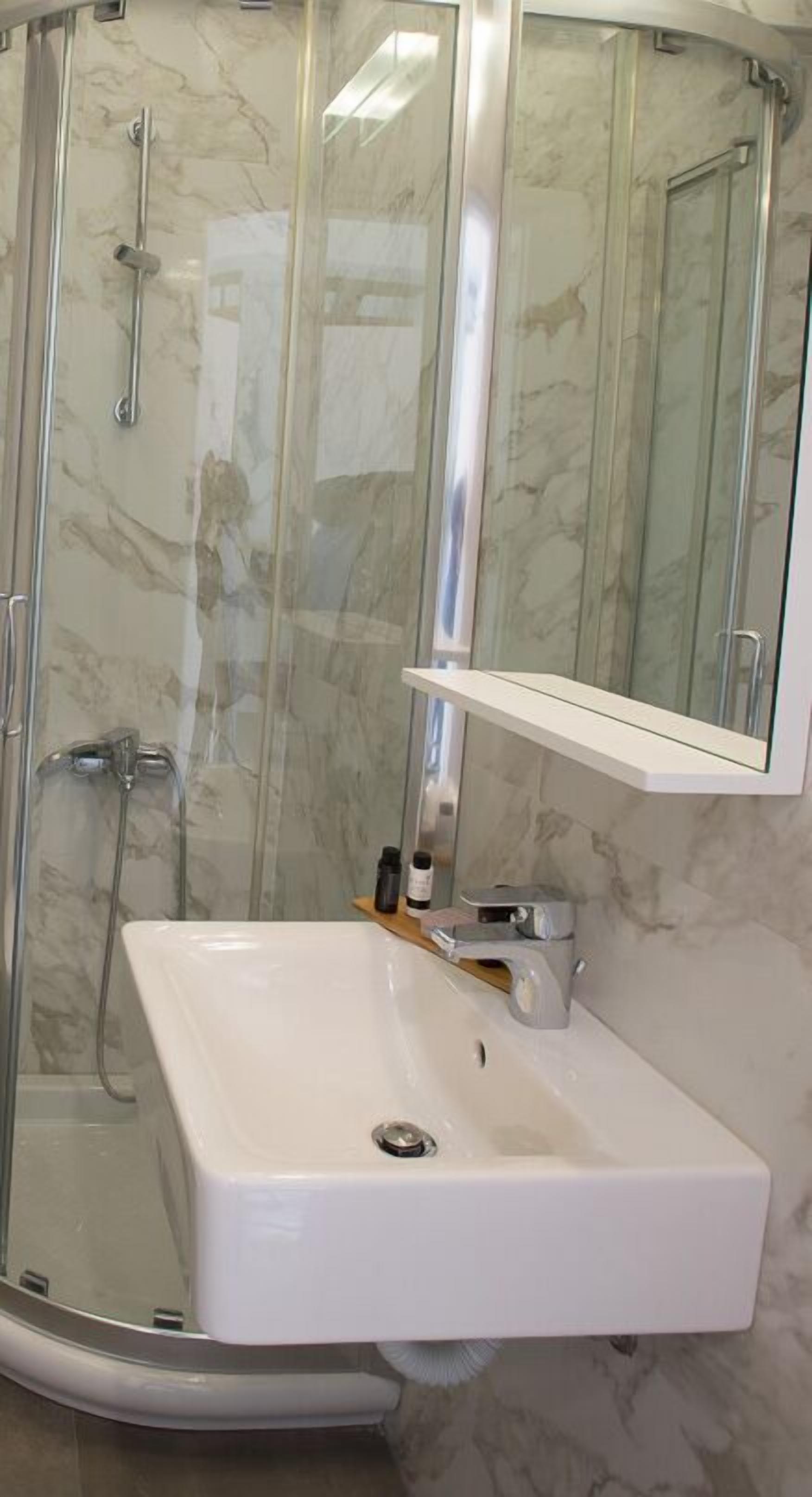 Une salle de bain moderne avec une douche à parois de verre, un lavabo blanc et un mur en marbre.