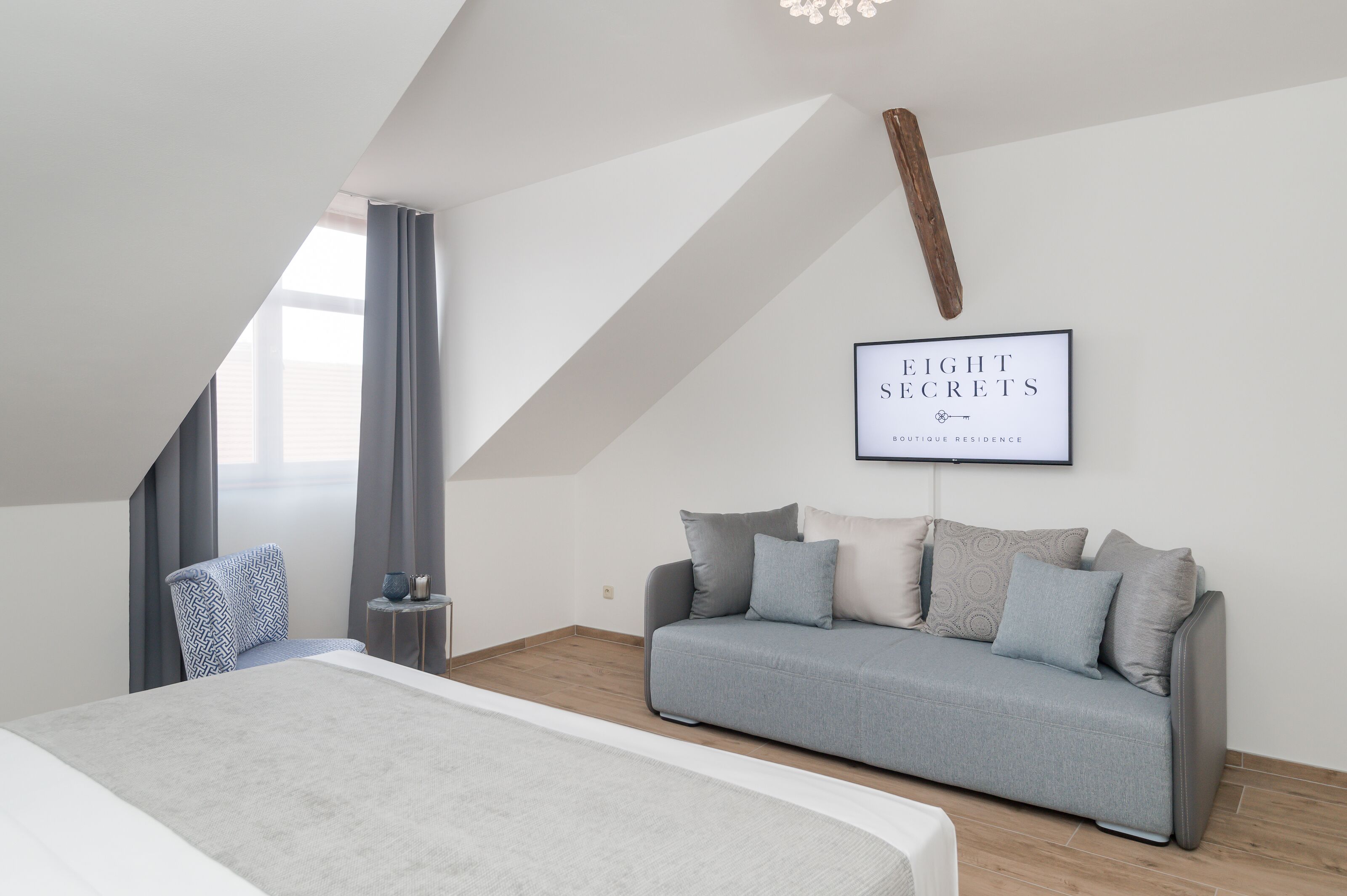 Un dormitorio moderno con cama, sofá gris, una mesita y televisor instalado en la pared.
