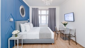 Un dormitorio moderno con una cama, una mesita con flores, un escritorio con sillas y una araña.