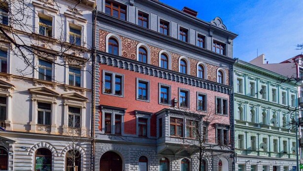 Un edificio de varios pisos con un estilo arquitectónico clásico, que presenta una combinación de fachadas de ladrillo y piedra, ventanas grandes y una entrada destacada con puerta de madera.