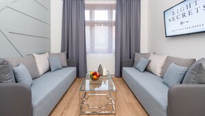 Una sala de estar moderna con dos sofás grises, una mesa de centro de vidrio con fruta y un ventanal con cortinas grises.