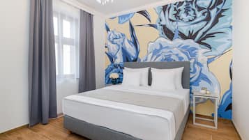 Un dormitorio con una cama grande, cortinas grises, un mural floral en la pared y una mesita de noche con un florero.
