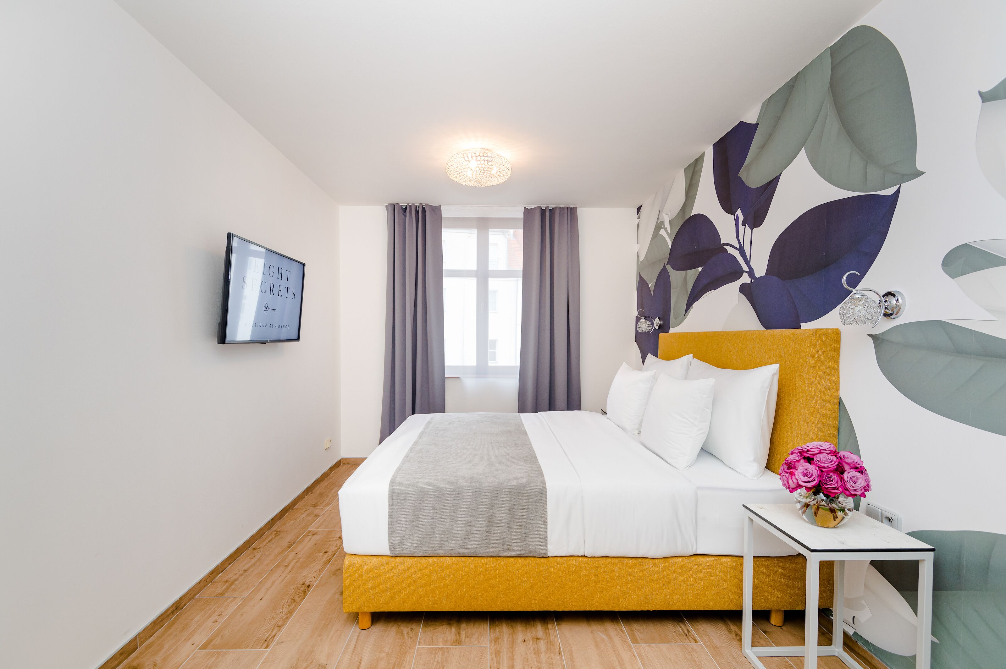 Ein modernes Hotelzimmer mit einem Bett, einem Nachttisch mit Blumenvase und einem großen Wandbild.