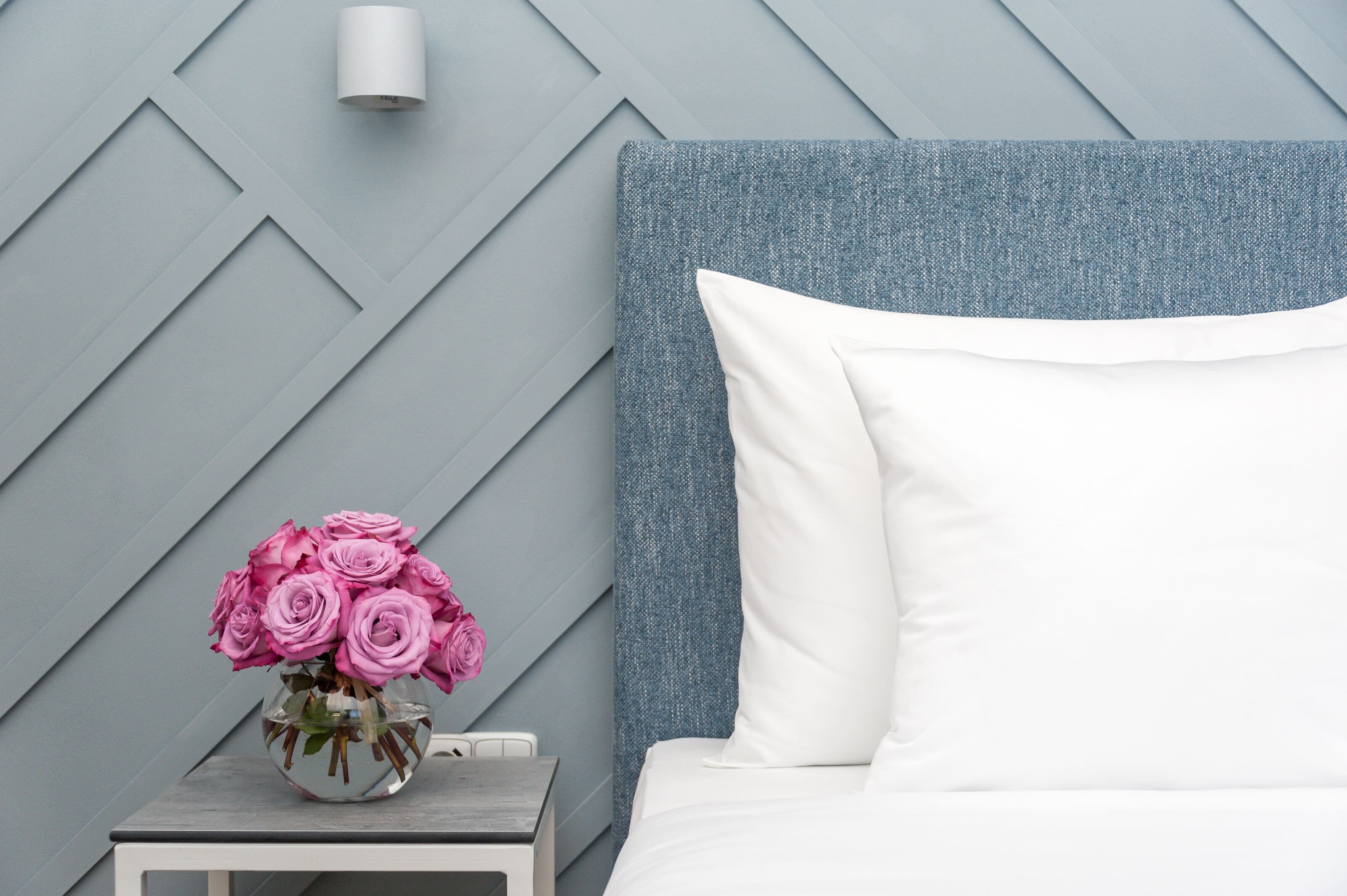 A neatly arranged bedroom with a bed, a nightstand, and a vase of pink roses.