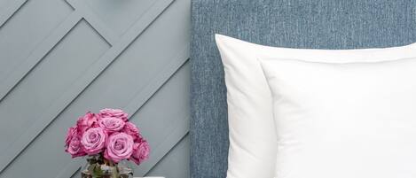 A neatly arranged bedroom with a bed, a nightstand, and a vase of pink roses.