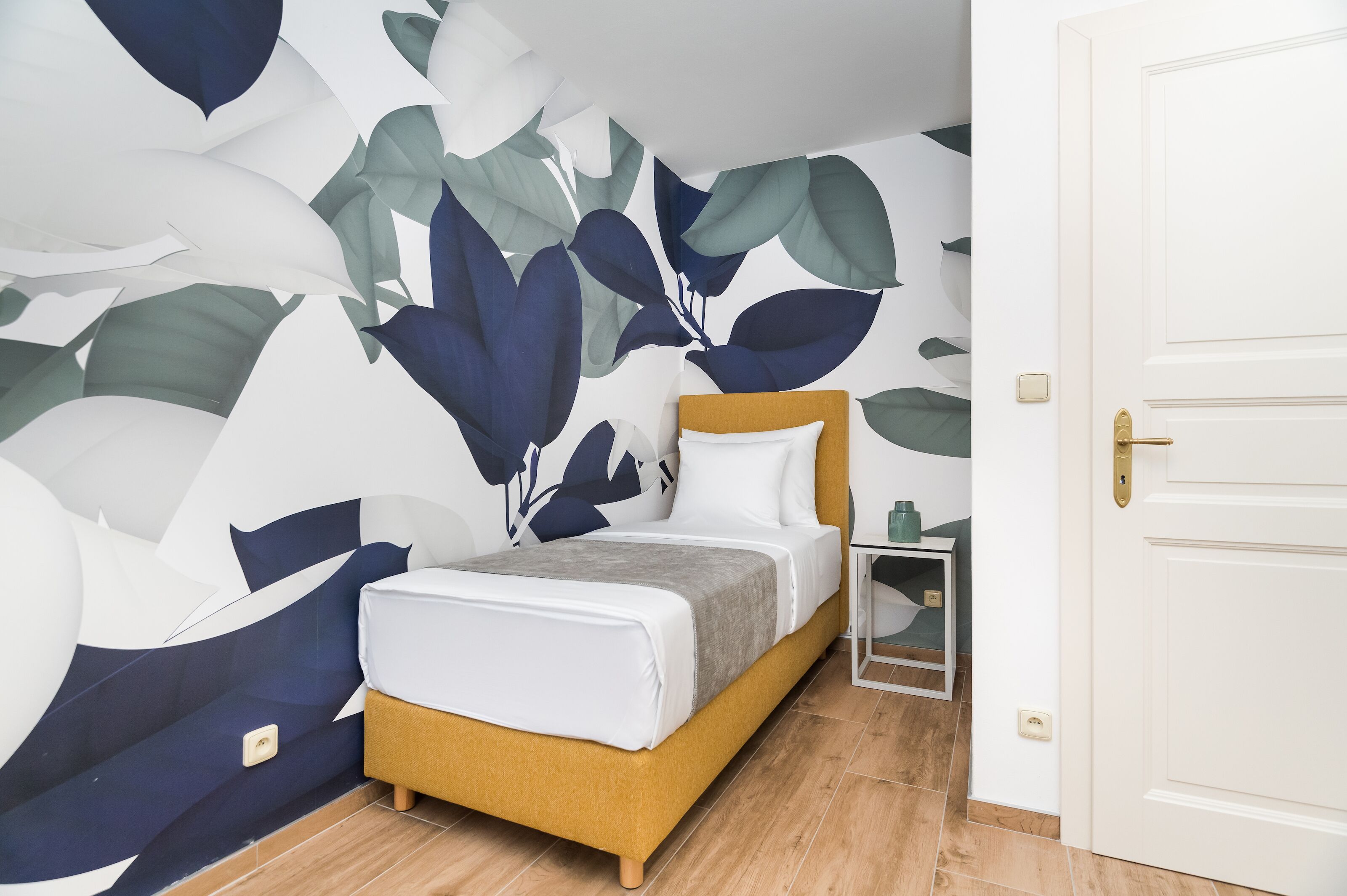 Un dormitorio con cama, mesita de noche y un muro con diseño de hojas.