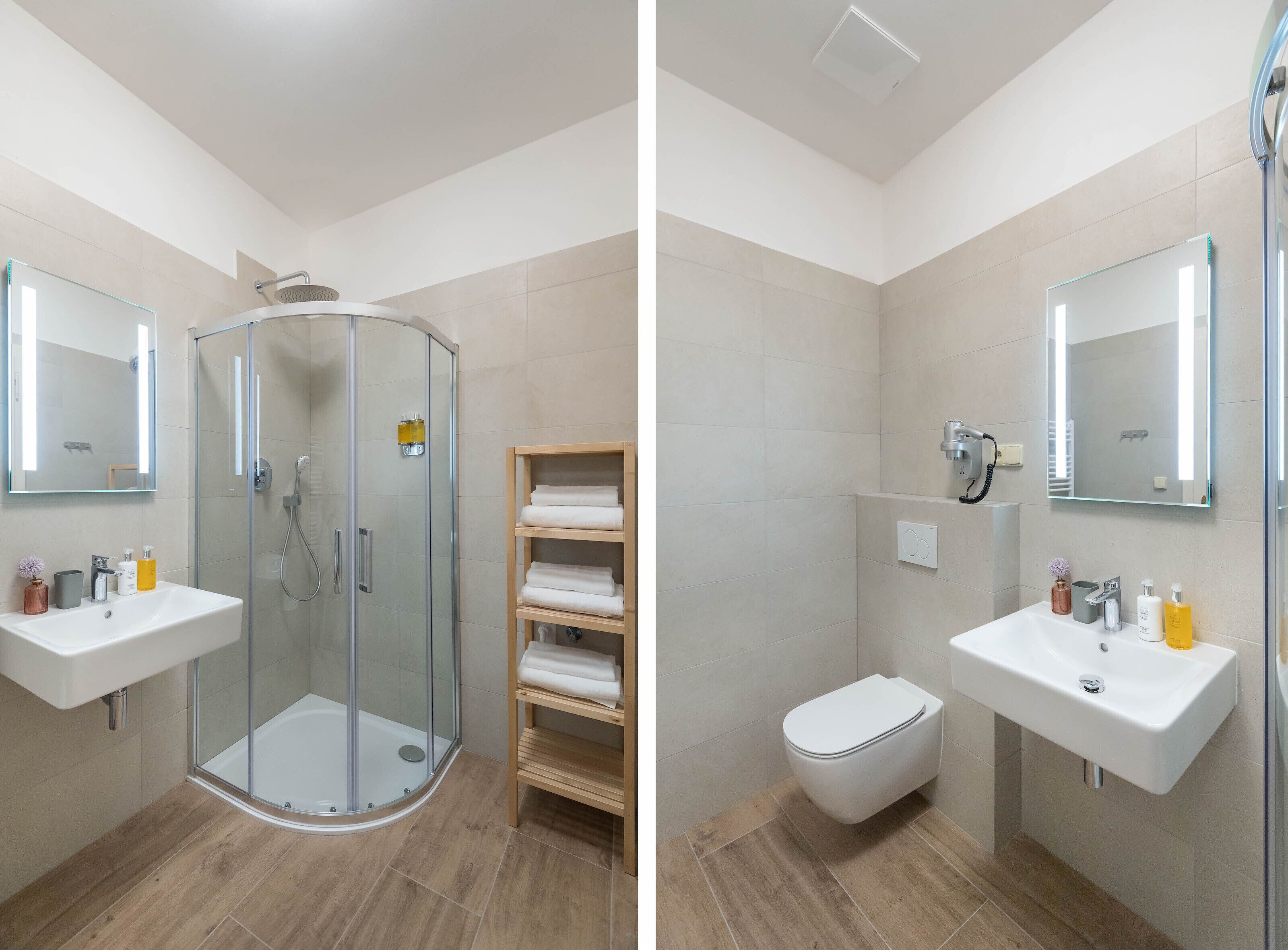 Une salle de bain moderne avec une douche à parois de verre, deux lavabos, des toilettes et une étagère en bois où sont posées des serviettes.