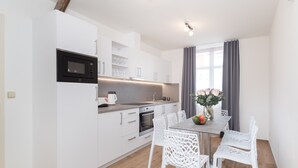 Una cocina moderna con armarios blancos, un microondas integrado y una zona de comedor con sillas y una mesa blancos.
