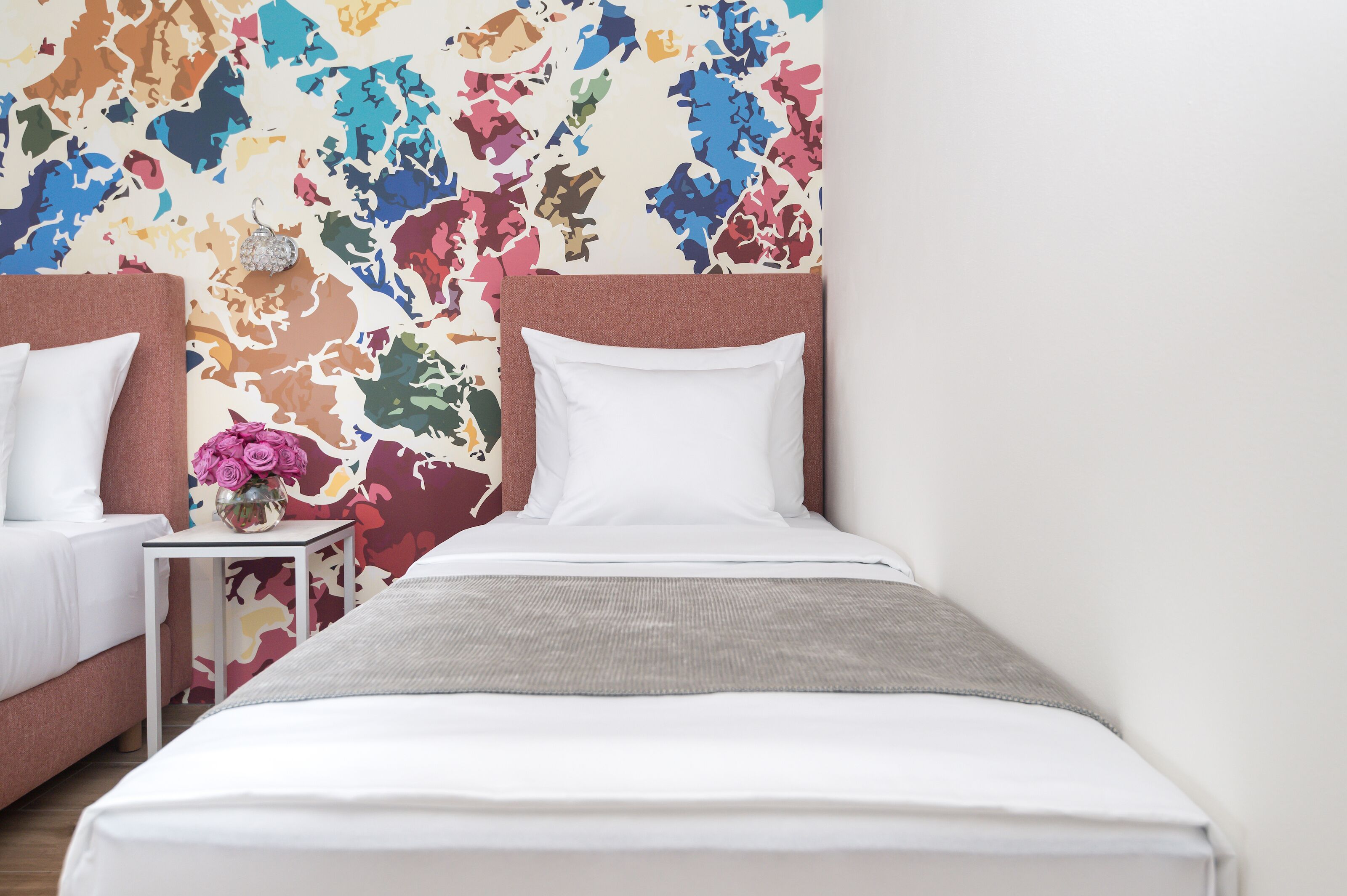 Una habitación de hotel con una cama, dos mesitas de noche, un muro decorativo y un jarrón con flores.