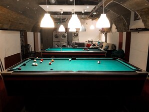 Une table de billard avec des billes, un éclairage suspendu et, en arrière-plan, un lave-linge.