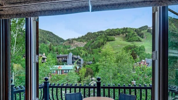 A balcony with a leather sofa and two chairs, a patterned rug, and a view of a green landscape with buildings.