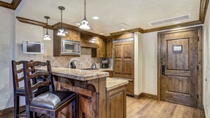 A kitchen with wooden cabinets, a built-in island with bar stools, a microwave, and pendant lighting.