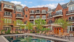 A brick building with multiple balconies and a swimming pool area with lounge chairs.