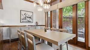 A dining area with a large wooden table, cushioned chairs, and a hanging light fixture.