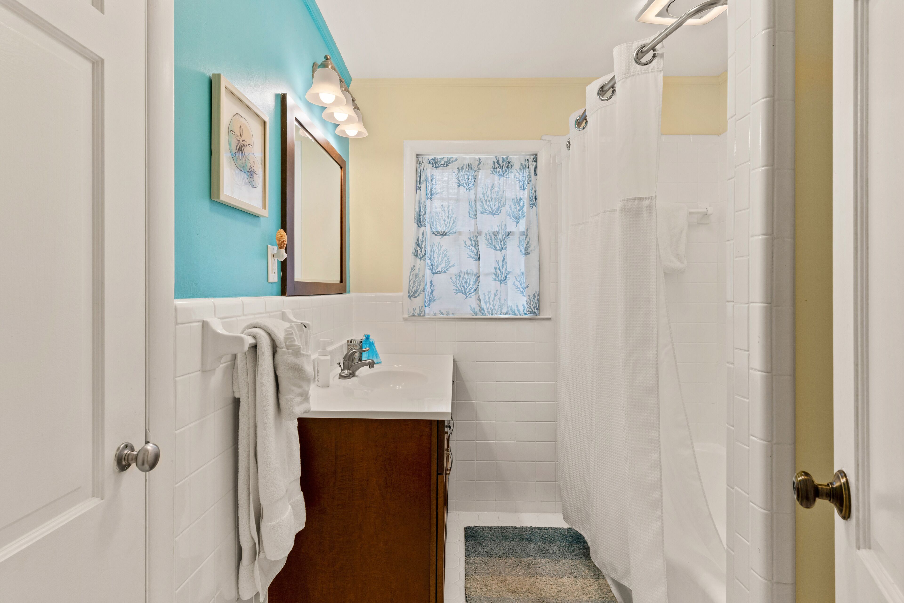 A bathroom with a white sink, a mirror, a towel rack, a shower curtain, and a small window with a blue pattern.