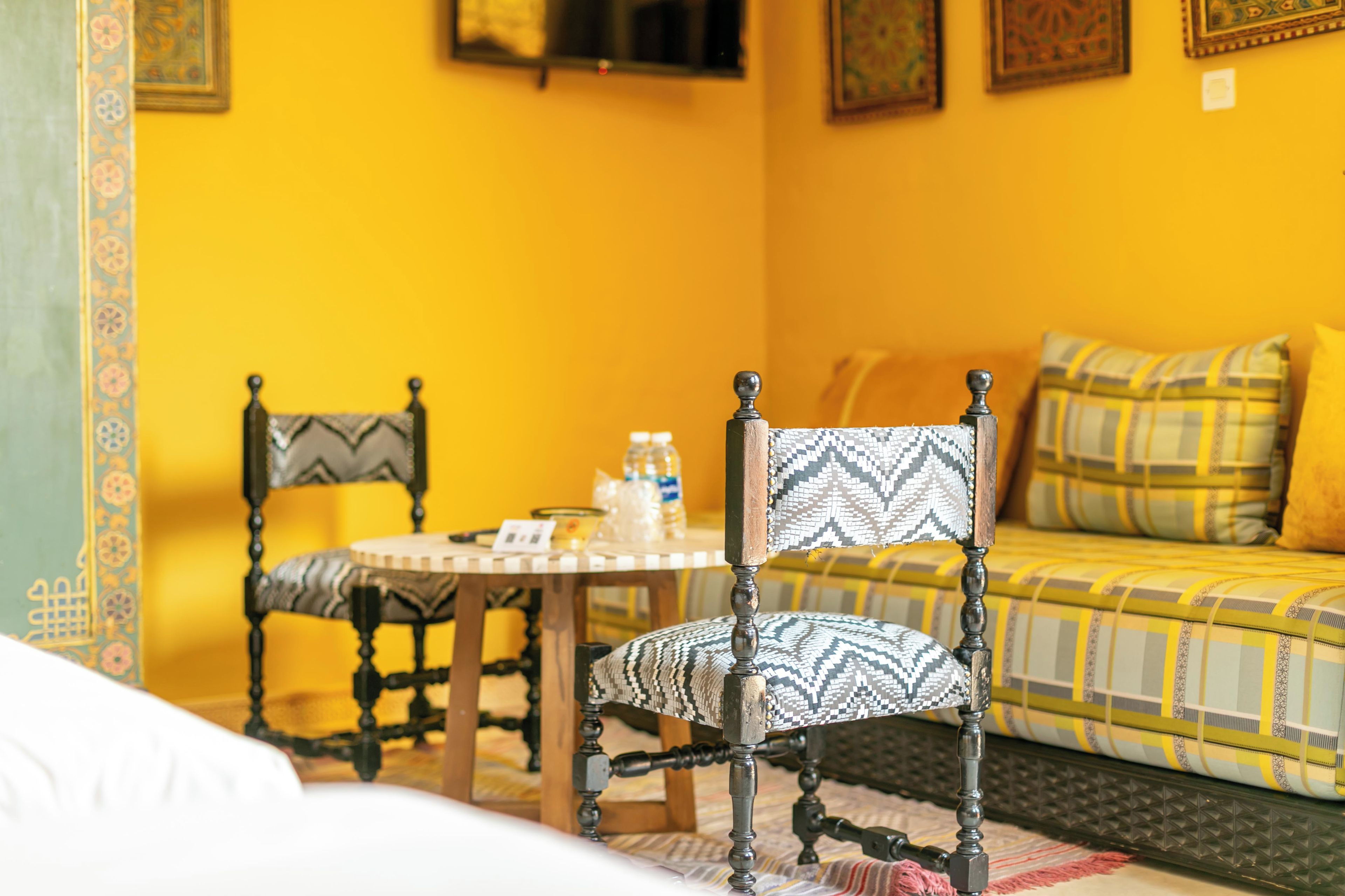 Une pièce comprenant un lit, une chaise, une table avec une bouteille et un canapé agrémenté de coussins à motifs.