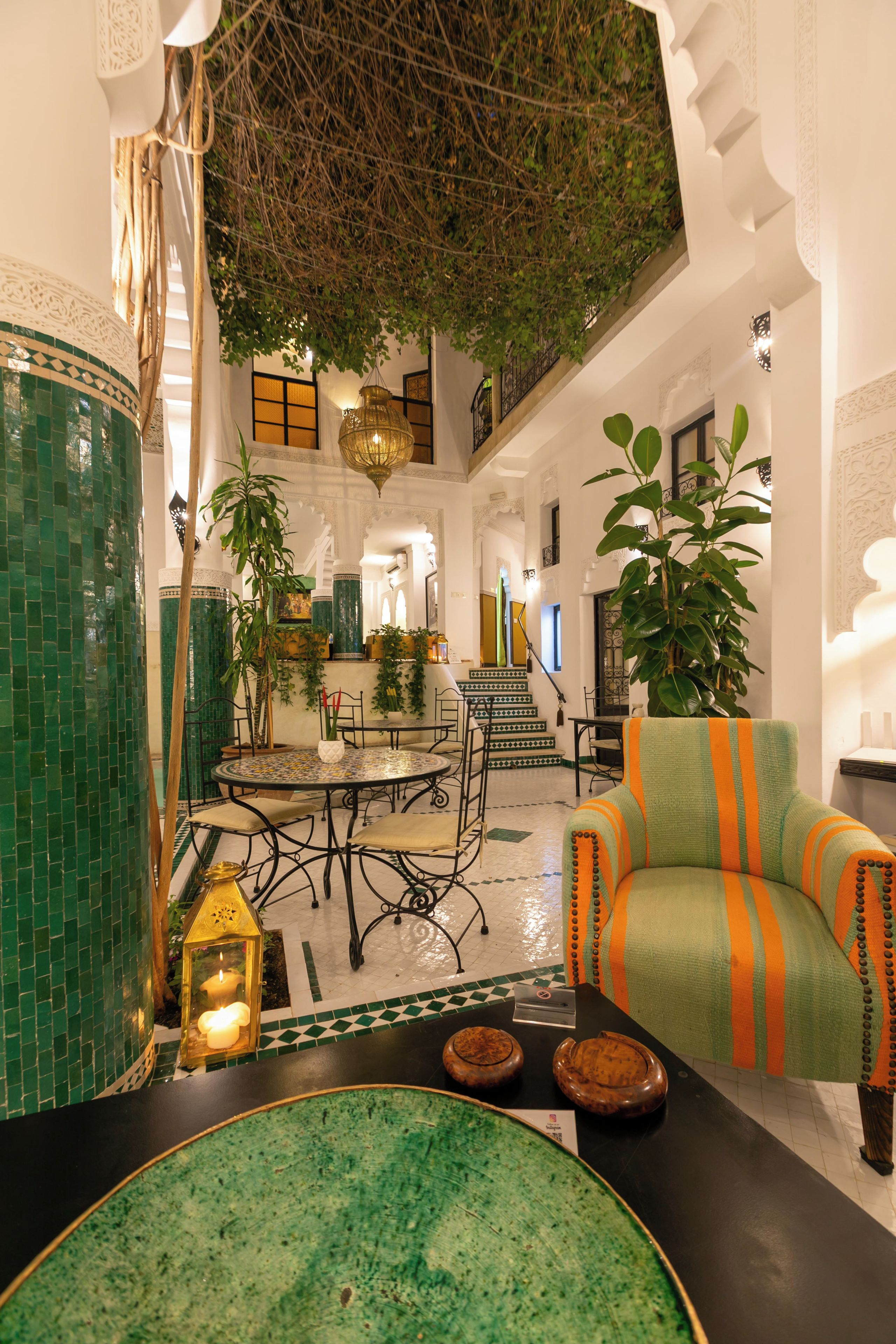 Un espacio interior amplio con techo alto, paredes de azulejos verdes y una zona de estar central con una mesa redonda y sillas.
