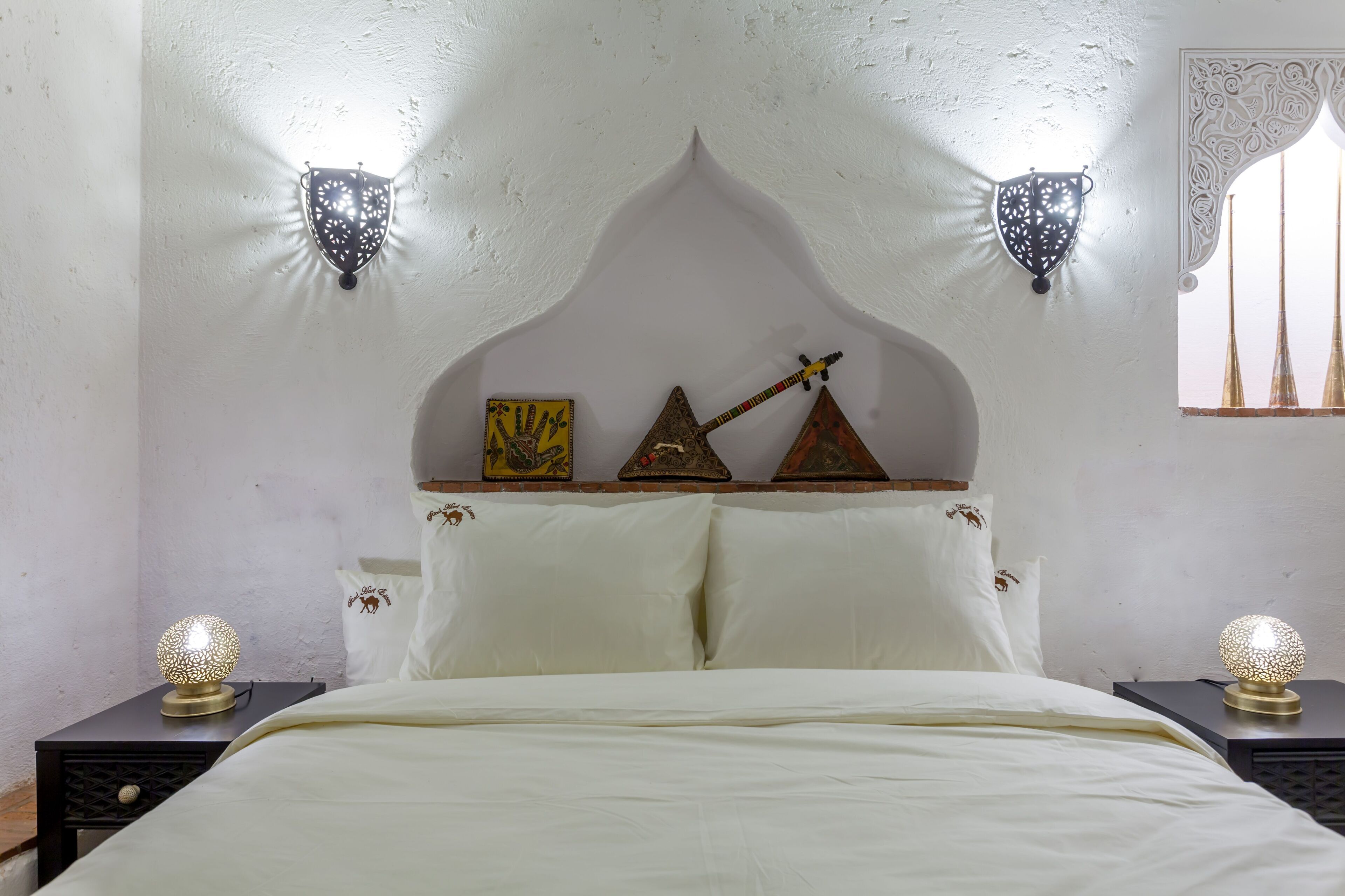 Una cama con cabecera blanca, dos lámparas fijadas a la pared y elementos decorativos como una guitarra y un escudo.