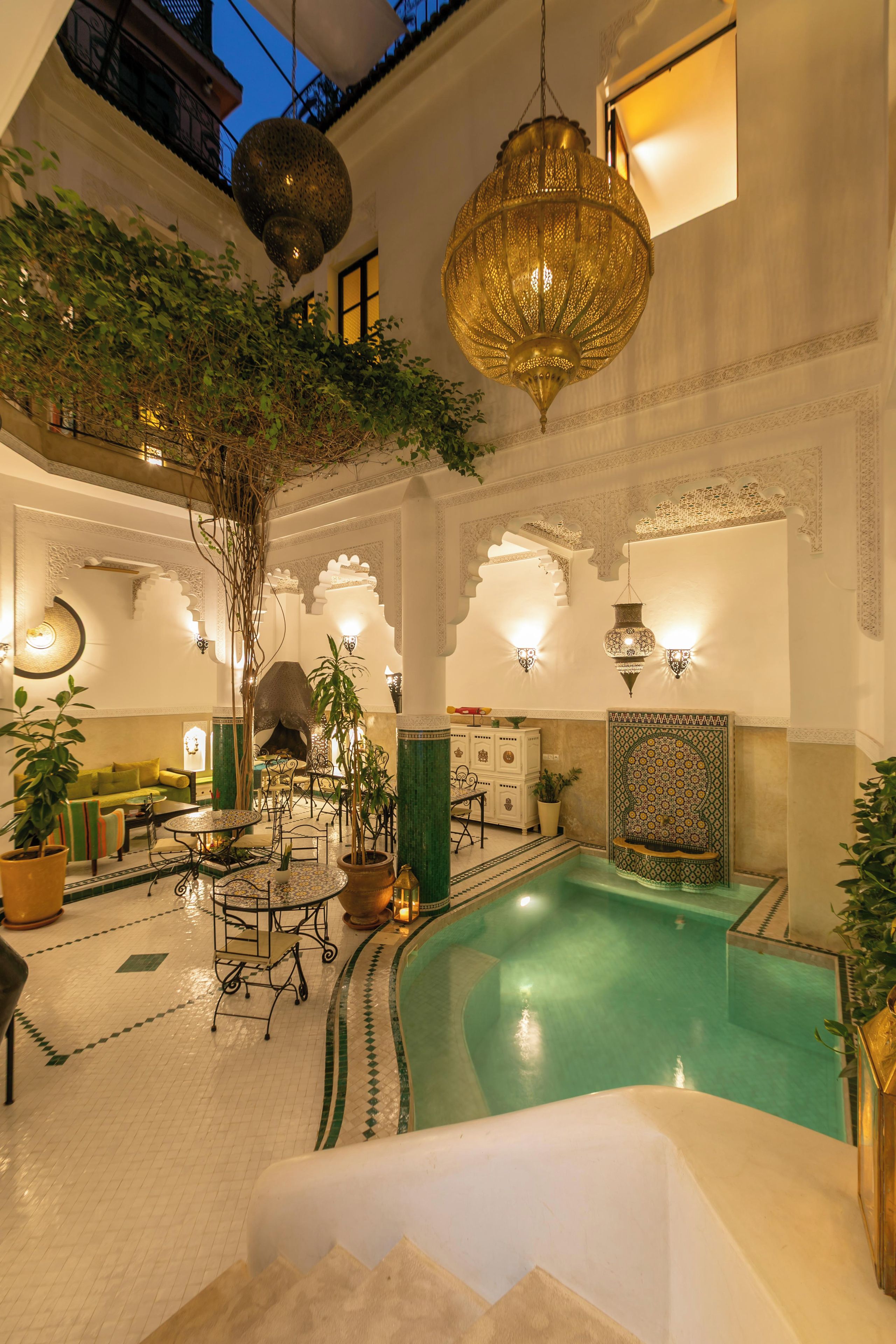 Una piscina interior con suelo de baldosas, rodeada de zonas de estar y una pared decorativa con diseños intrincados.
