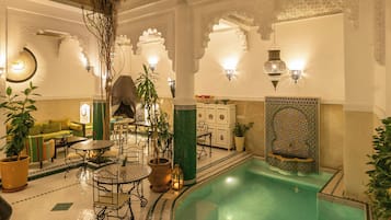 Una piscina interior con suelo de baldosas, rodeada de zonas de estar y una pared decorativa con diseños intrincados.