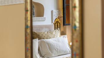 Un dormitorio con cama, almohadas, mesita de noche, espejo y una obra de arte colgada en la pared.