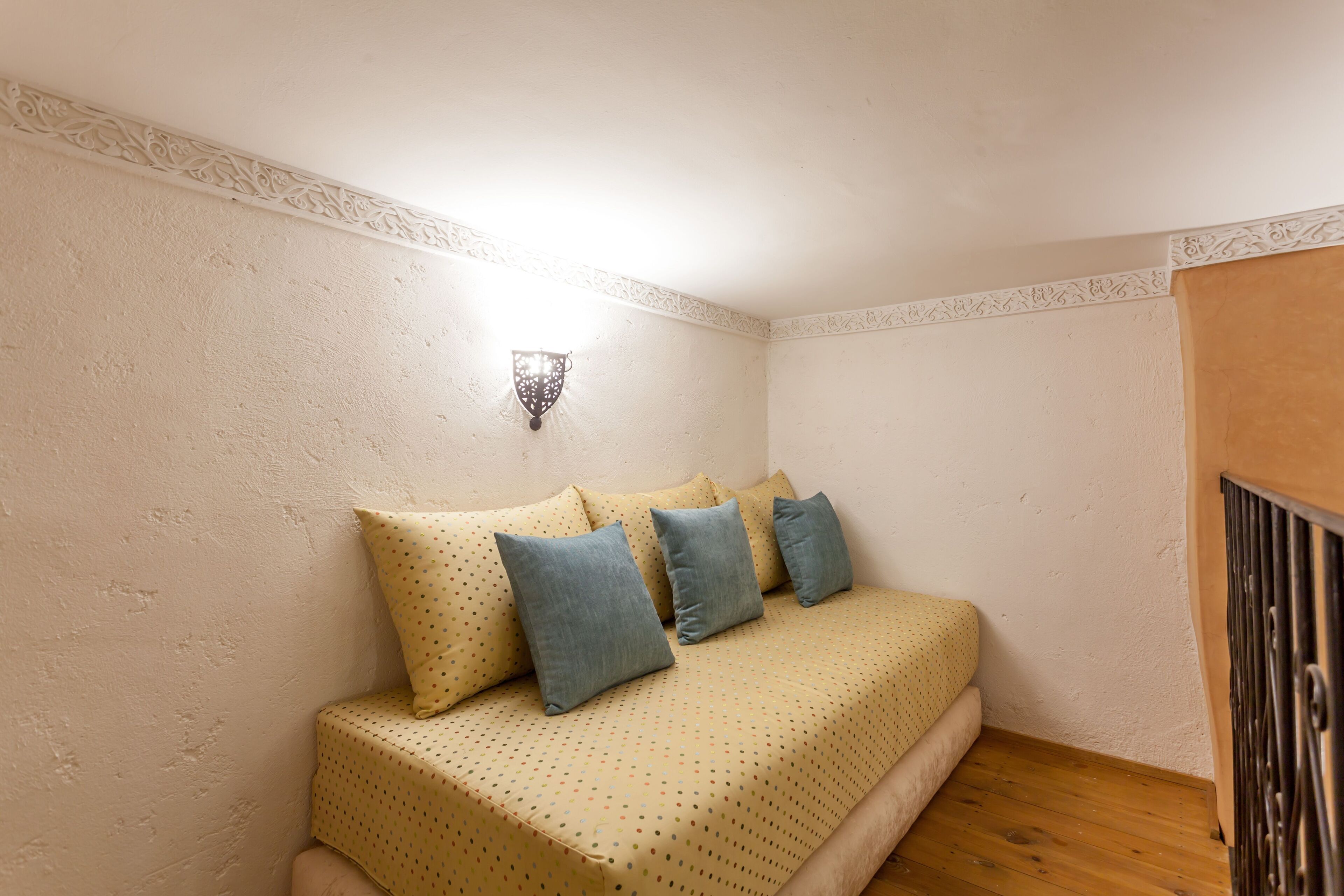 Une petite chambre à coucher accueillante, avec un lit, des oreillers, une lampe fixée au mur et un plancher en bois.