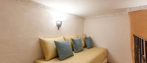 A small, cozy bedroom with a bed, pillows, a wall-mounted light, and a wooden floor.