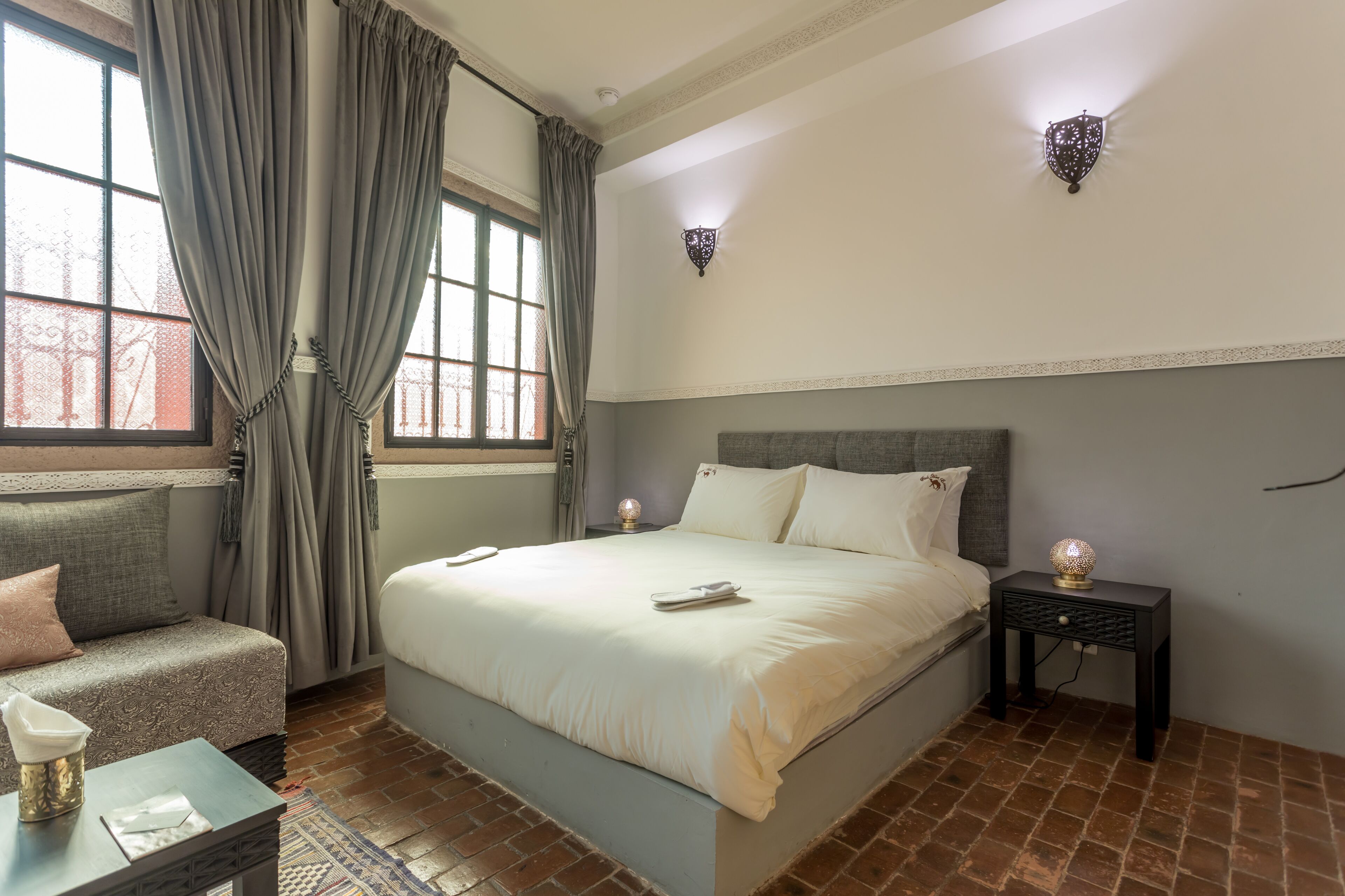 A neatly arranged bedroom with a bed, bedside tables, a sofa, and a window with curtains.