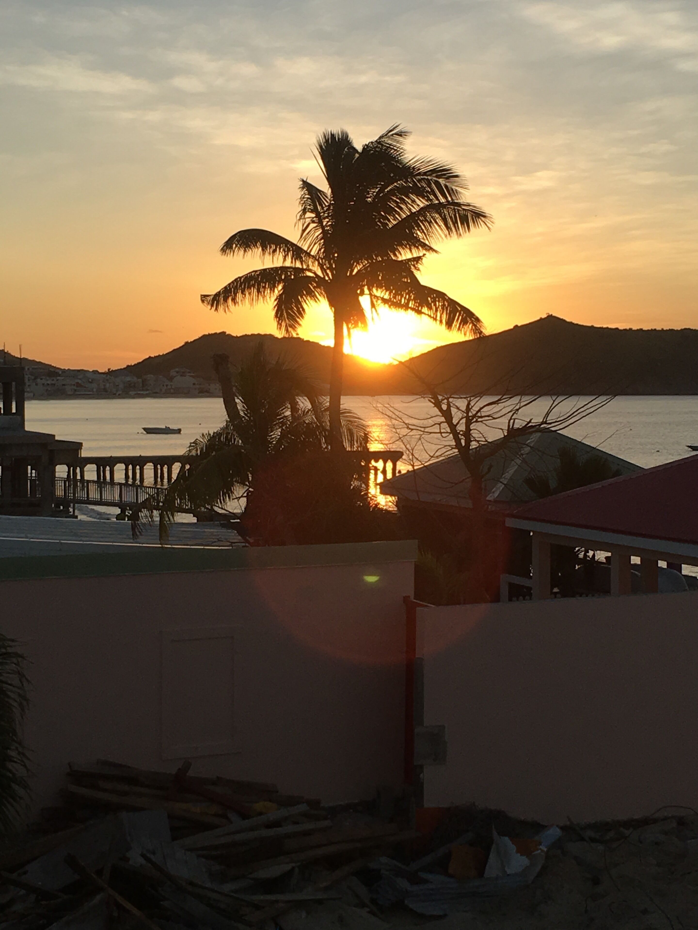 Auringonlasku vesistön yllä, etualalla palmu ja rakennus.