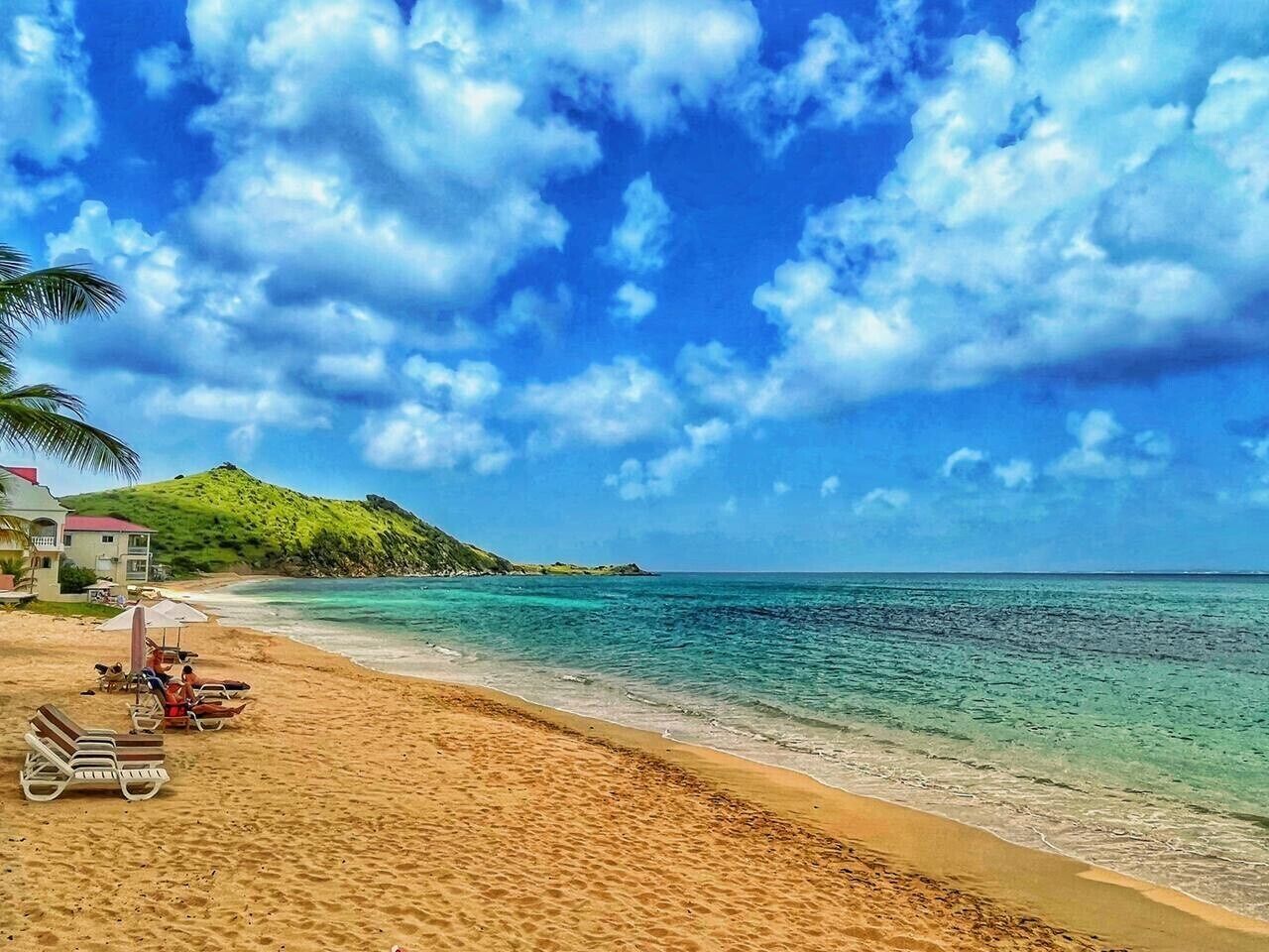 A beach with clear turquoise water, a sandy shore, and a few lounge chairs.
