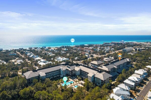 An aerial view of a coastal resort with multiple buildings, a clear view of the ocean, and a central swimming pool area. - Redfish Village M1-309 (Santa Rosa Beach)