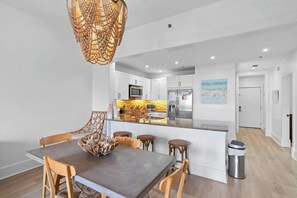 A modern kitchen with white cabinets, a central island, and a dining area with wooden chairs. - Redfish Village M1-309 (Santa Rosa Beach)